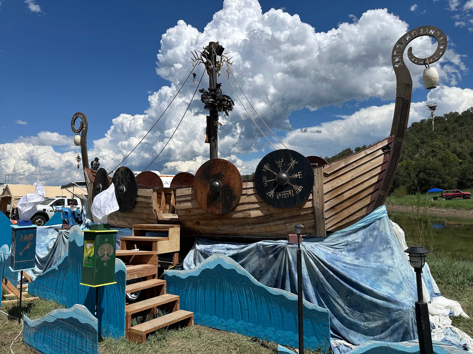 The ship on a grass field beneath tall cumulus, shields mounted along the hull and painted waves banked against its sides