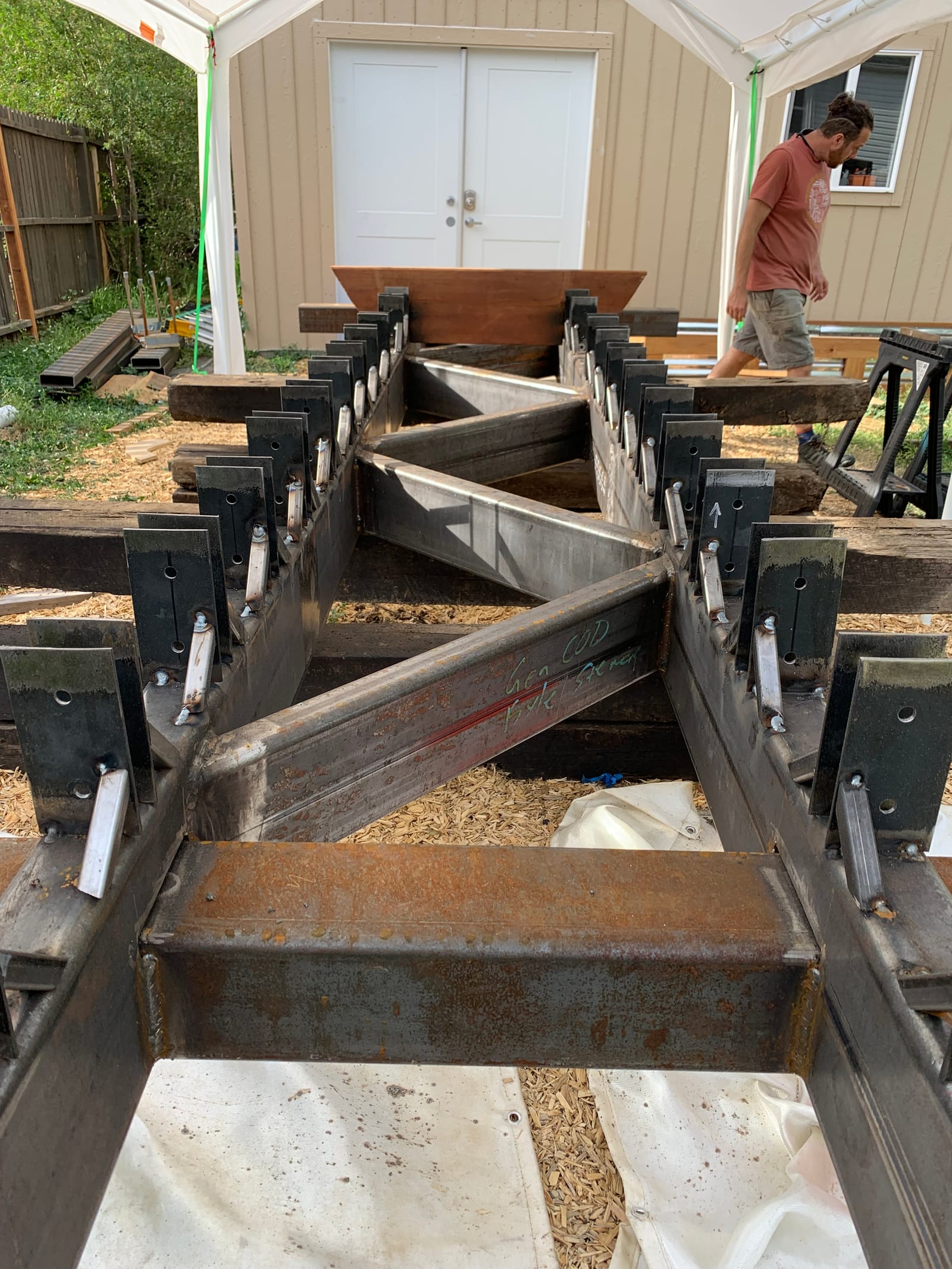 The welded steel keel frame clamped up outdoors under a canopy, dozens of C-clamps holding the cross members while the epoxy sets