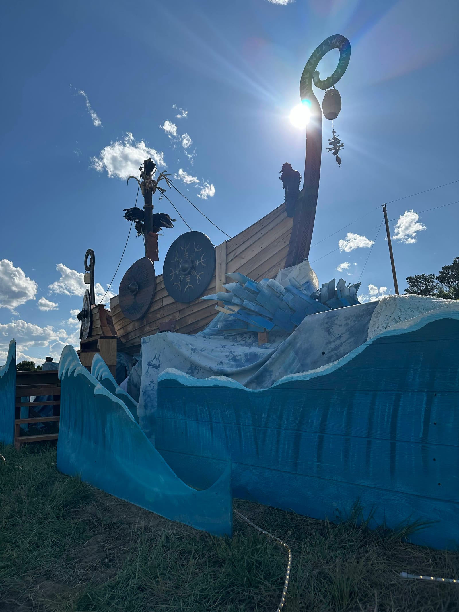 A low three-quarter view of the ship shot into the sun, the prow spiral silhouetted against a burst of light above the painted waves