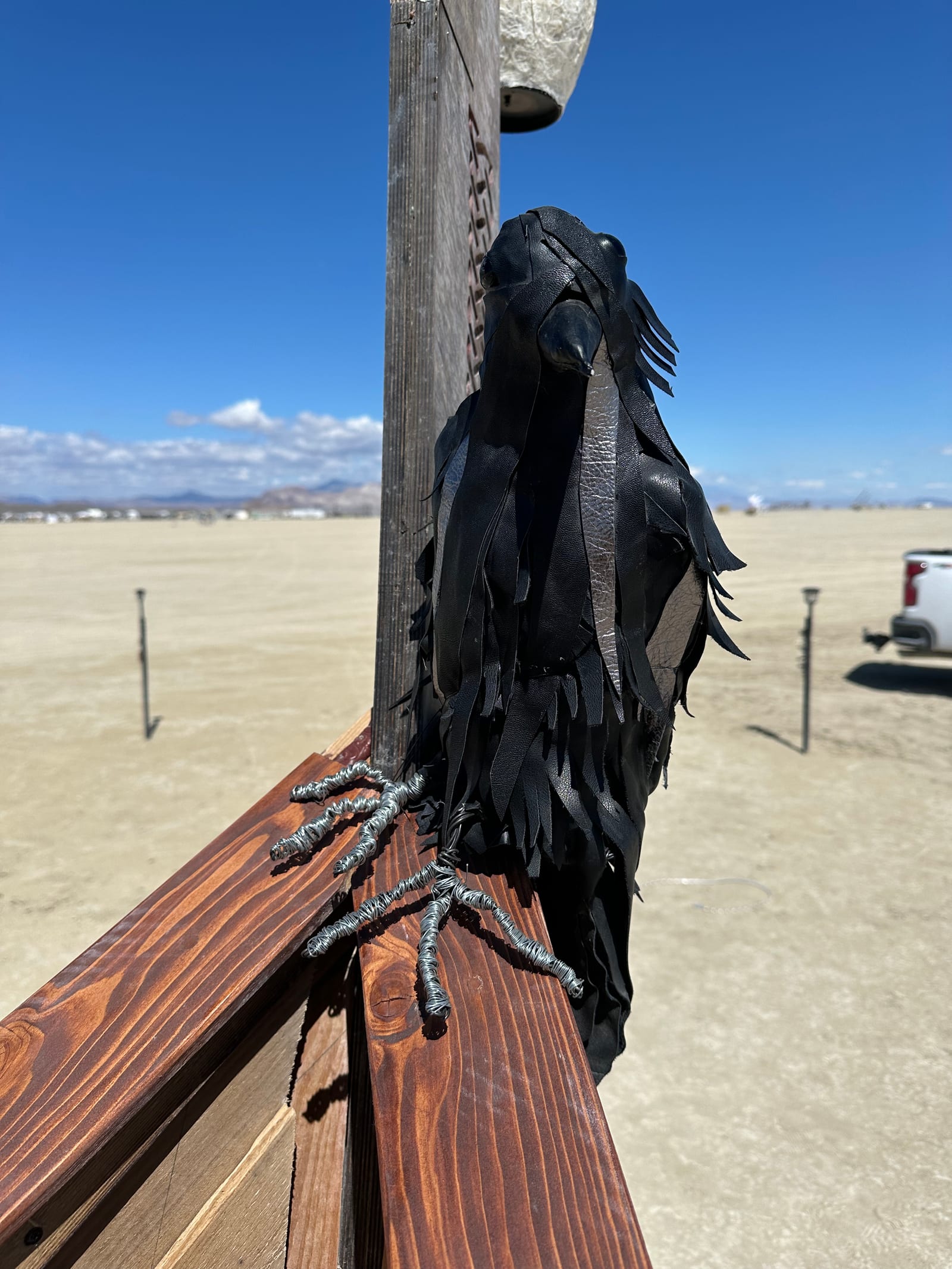 A raven built from cut black leather gripping the ship's rail with wire talons, the empty playa stretching out behind