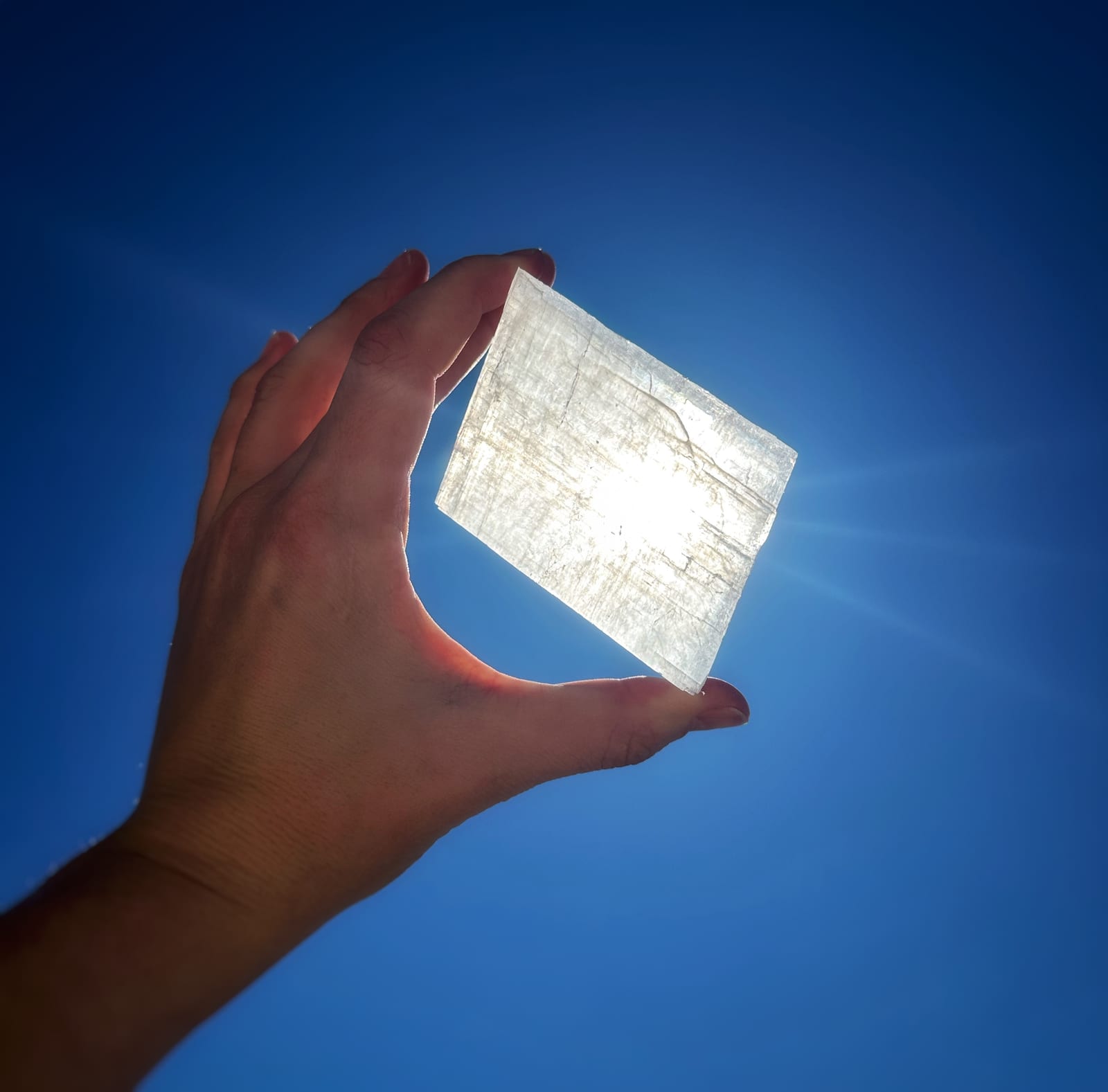 A hand holding a translucent panel up against a deep blue sky, sunlight blazing through the material