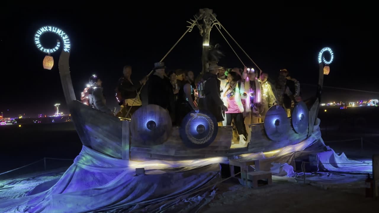 The lit ship at night with people aboard, a burst of flame above the deck